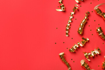 Shiny golden serpentine streamers and confetti on red background, flat lay. Space for text