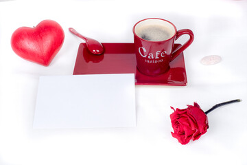 Red coffee cup with a white and blank gift card placed in front, surrounded by a red love heart and a red rose., white background. Love and valentine's day 