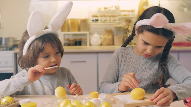 Happiness group of cute and adorable children prepare for easter. Cute little sisters with rabbit ears paint eggs for a bright Easter at home in the kitchen