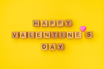 Wooden cubes with the phrase Happy Valentine's Day on an empty colorful yellow background. Words of love are made of letters from wood for Valentines Day greeting romantic postcard