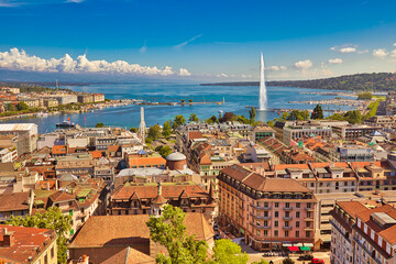 Geneva skyline cityscape, French-Swiss in Switzerland. Aerial view of Jet d'eau fountain, Lake Leman, bay and harbor from the bell tower of Saint-Pierre Cathedral. Sunny day blue sky. - 410393216