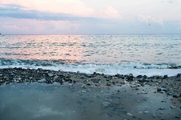 A beautiful cloudy sunset over the beach with a pebbly foreshore with a puddle after a rain.