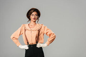 pretty woman in fashionable vintage clothes posing with hands on hips isolated on grey