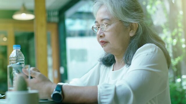 Active senior retired Asian business woman enjoy working on her own online small business and relaxing in a coffeeshop on a bright sunny day