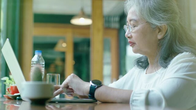 Active senior retired Asian business woman enjoy working on her own online small business and relaxing in a coffeeshop on a bright sunny day