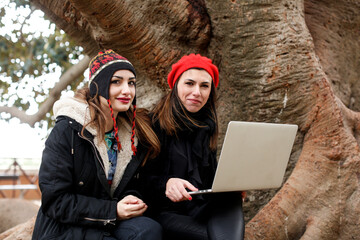 due ragazze more vestire di nero con copri capo colorati lavorano al computer vicino a un albero in...