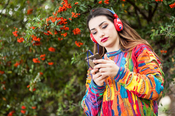 Ragazza mora vestita con un maglione colorato ascolta della musica con delle cuffie auricolari rosse