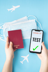 Person holding a smartphone showing copyright free negative coronavirus test and a passport with the other hand, on a blue background with white planes and masks