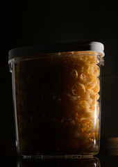 Close up view of jar full with Rotelle Wagon wheel-shaped pasta against dark background