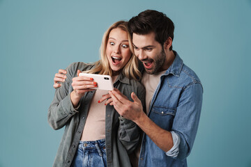 Young surprised man and woman hugging and using mobile phone