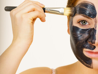 Female applying black mud facial mask