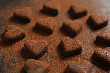 Fototapeta na wymiar Beautiful heart shaped chocolate candies with cocoa powder on black table, closeup