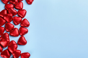 Heart shaped chocolate candies in red foil on light blue background, flat lay. Space for text
