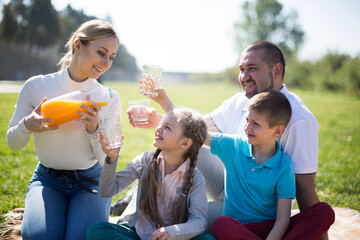 family of parents with two children drinking orange juice on a picnic in the park