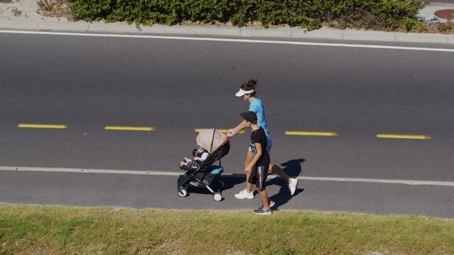 Mother with children and baby stroller walks down the street along the road.