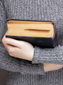 vertical image of a woman in a gray sweater holds an old book in her hands and hugs her