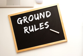 Text GROUND RULES written in chalk on a slate board. Office desk.