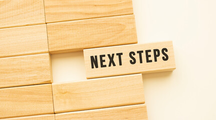 NEXT STEPS text on a strip of wood lying on a white table.
