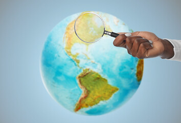 investigation, discovery and search concept - hand with magnifying glass over earth planet on blue...