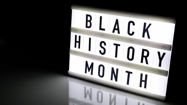 Lightbox with text BLACK HISTORY MONTH on dark black background with mirror reflection. Message historical event. 4k Video. Zoom in
