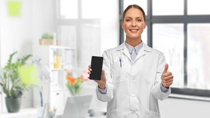 Naklejka na ściany i meble medicine, profession and healthcare concept - happy smiling female doctor showing smartphone and thumbs up over medical office at hospital on background