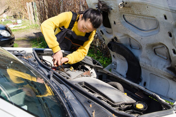 Asian female mechanic dressed in special clothes fixing a car near the house