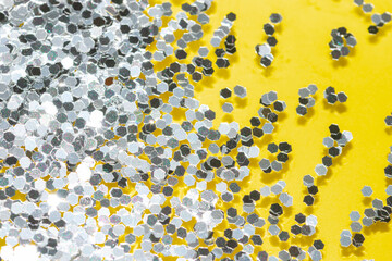 transparent liquid with silver glitter pouring over a pastel yellow background