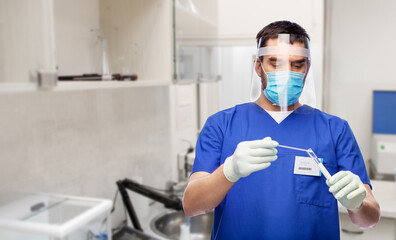 Fototapeta na wymiar healthcare, profession and medicine concept - doctor or scientist in blue uniform, face mask for protection from virus, face shield and gloves with cotton swab and test tube over laboratory background