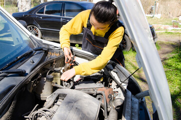 Asian female mechanic dressed in special clothes fixing a car near the house