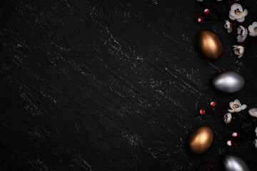 Golden and silver Easter eggs with flower on black background.