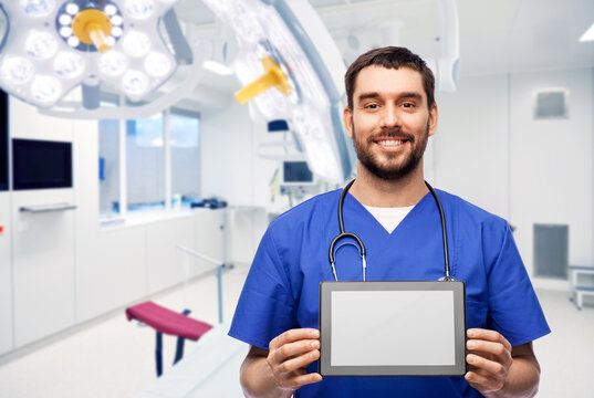 medicine, healthcare and technology concept - happy smiling doctor or male nurse in blue uniform with stethoscope showing tablet pc computer over operating room at hospital on background