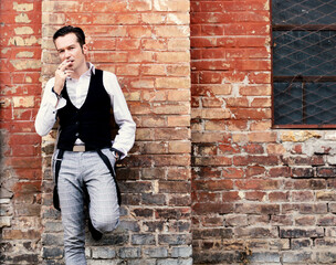 Fototapeta na wymiar Self-confident man smoking cigarette while leaning on brick wall.