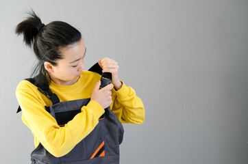 Asian Female construction worker dressed in special clothes with a cordless screwgun, a construction tool isolated on grey background