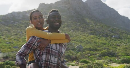 African american man giving piggyback ride to his wife while trekking in the mountains - Powered by Adobe