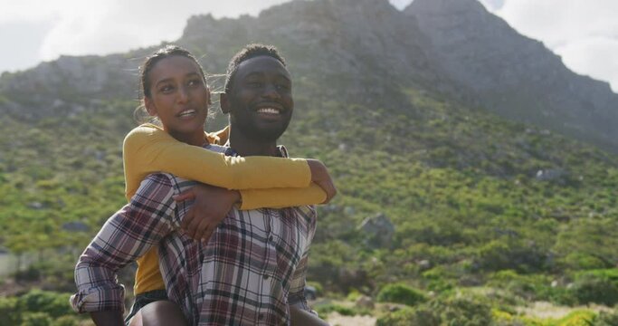 African american man giving piggyback ride to his wife while trekking in the mountains