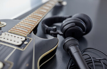 leisure, music and musical instruments concept - close up of bass guitar, microphone and headphones on black table