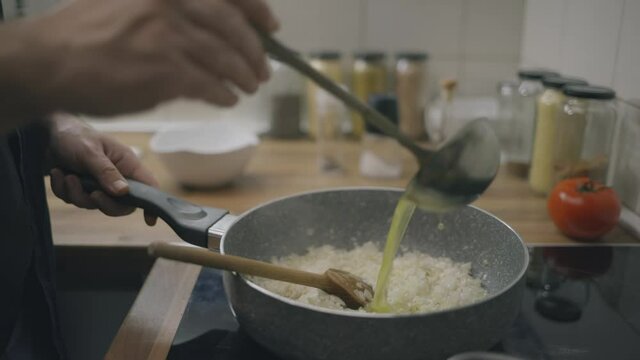 Chef pouring chicken stock in risotto