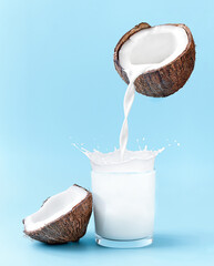 Cracked coconut with splashes of milk on blue background. coconut milk is poured into the glass