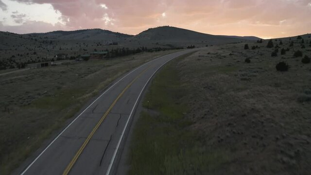 Aerial fly over drone footage with oncoming traffic on Montana Mountain Pass Road, Montana, USA with pink clouds in the horizon