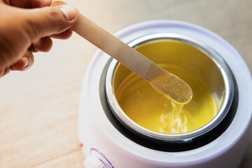 Yellow hot liquid wax for depilation on a wooden stick. The concept of depilation, beauty, skin care
