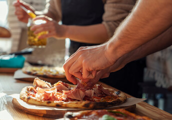 Close-up of a man and a woman's hands are preparing pizza in the kitchen in a restaurant, laying out the meat and oiling. on a sunny day