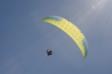 backlit paragliding flight with sun and blue sky