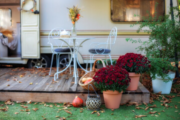 Table and chairs with tea set  placed outside cozy retro caravan trailer in garden. Cozy wooden RV...