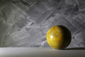 Sfera gialla dipinta ad effetto marmorizzato,  isolata su fondo grigio spatolato