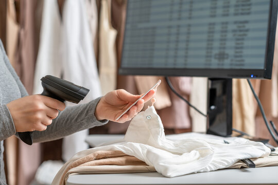 A warehouse woman employee accepts clothes using barcode scanner reading a bar code from price tag of female blouse and adds to the computer base.