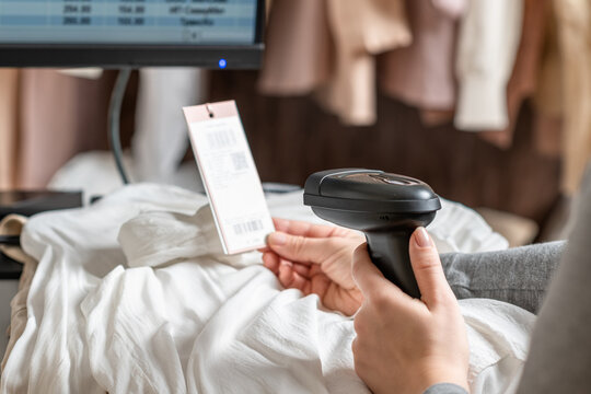 A warehouse woman employee accepts clothes using barcode scanner reading a bar code from price tag of female blouse and adds to the computer base.