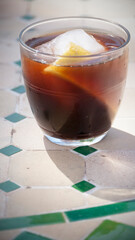 Café con hielo y cáscara de limón en vaso de cristal sobre mesa de jardín