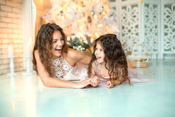 family, christmas, holidays and people concept - happy mother and a cheerful little daughter, next to a decorated white Christmas tree