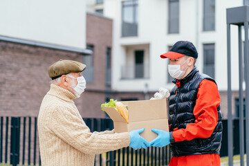 Young male volunteer in mask gives an elderly man boxes with food near her house. Son man helps a single elderly father. Family support, caring. Quarantined, isolated. Coronavirus covid-19. Donation