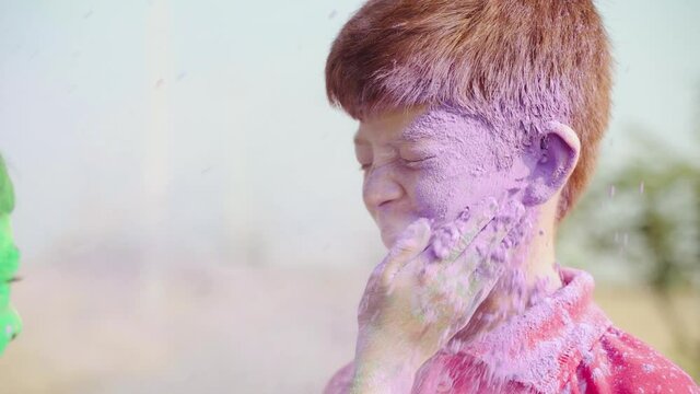 Close up of Hands applying or slapping with holi color powder to smiling Caucasian kid during holi festival celebration - Concept holi festival celebration in different part of the world